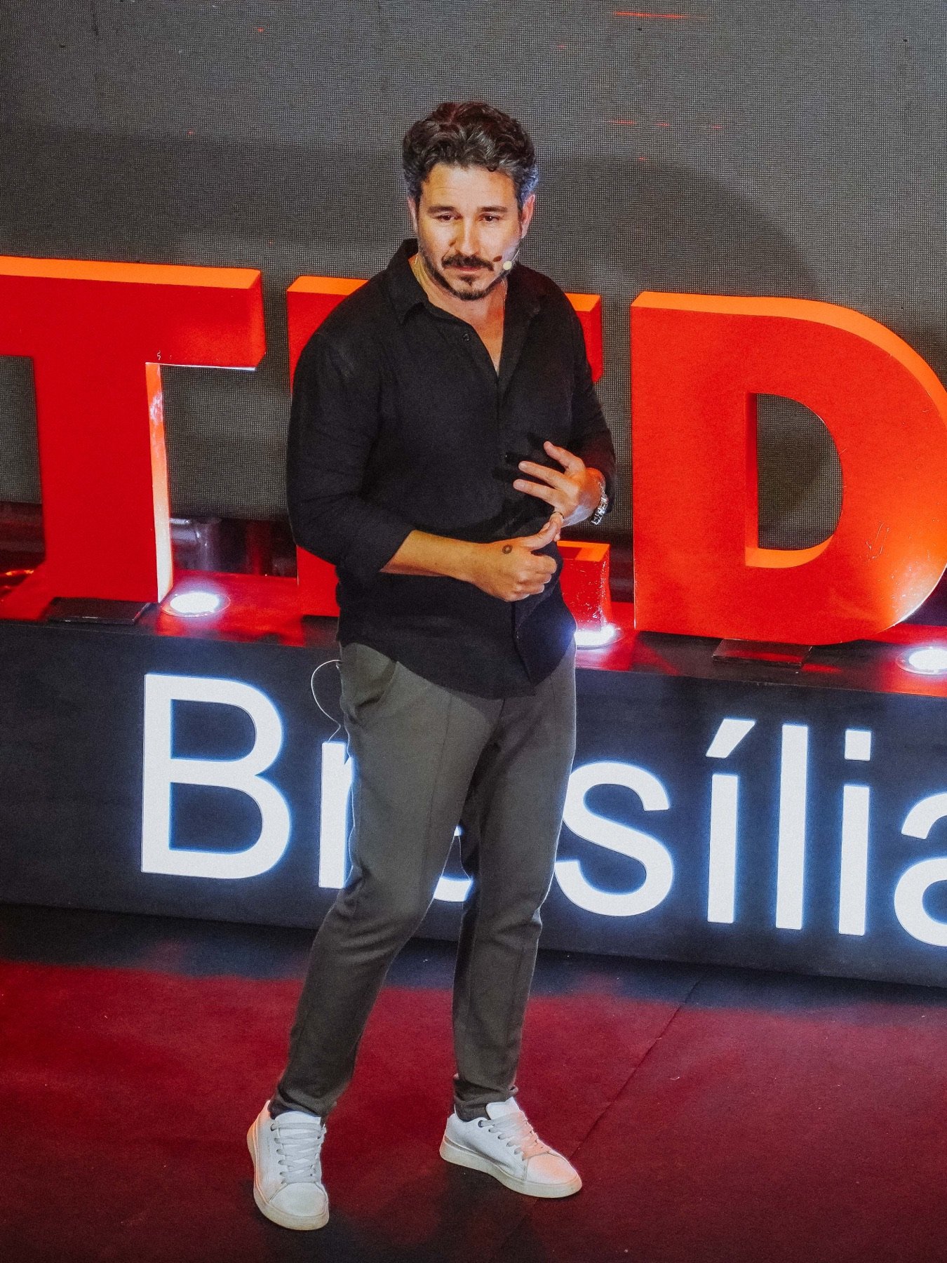Dan Rocha de corpo inteiro no palco, em frente ao letreiro TEDx Brasília